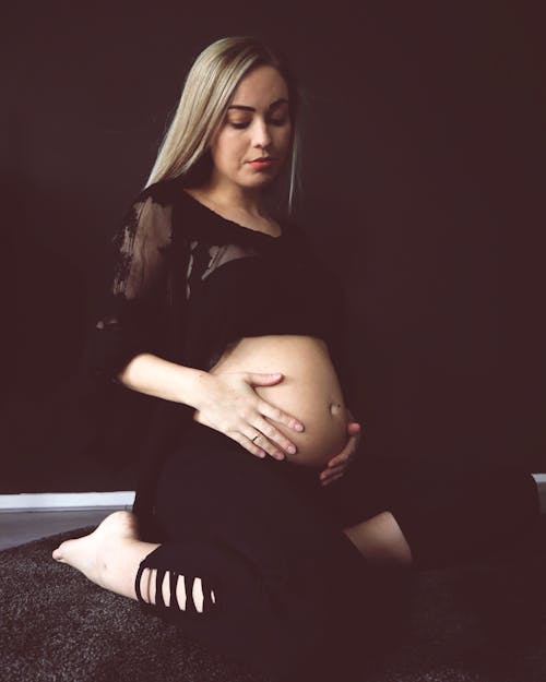 Photo of Pregnant Woman in Black Outfit Kneeling on Floor While Looking Down