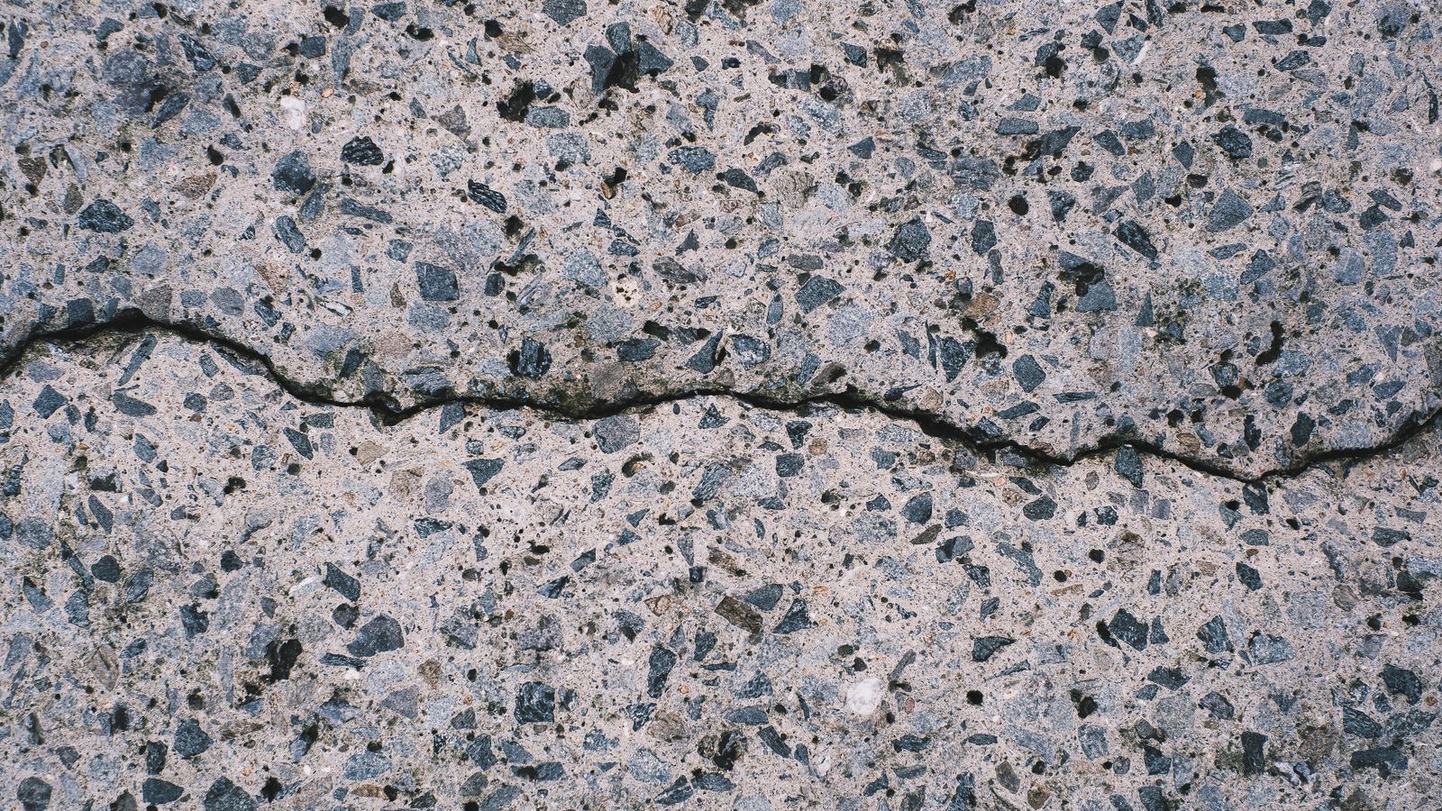 Close-up of a crack running across a stone-aggregate concrete surface