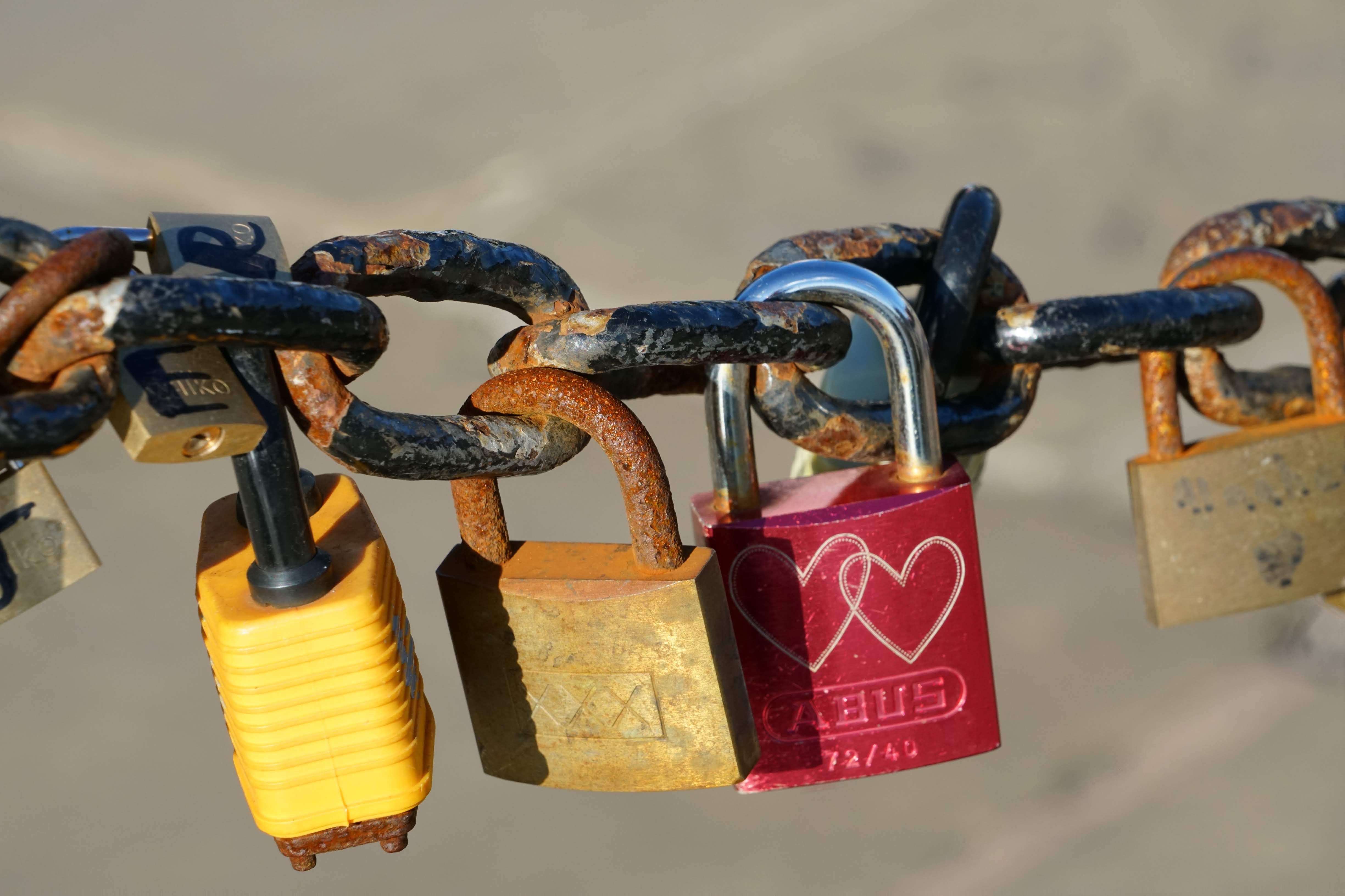 Close-up image of various padlocks attached to a rusted chain, symbolizing eternal love ou