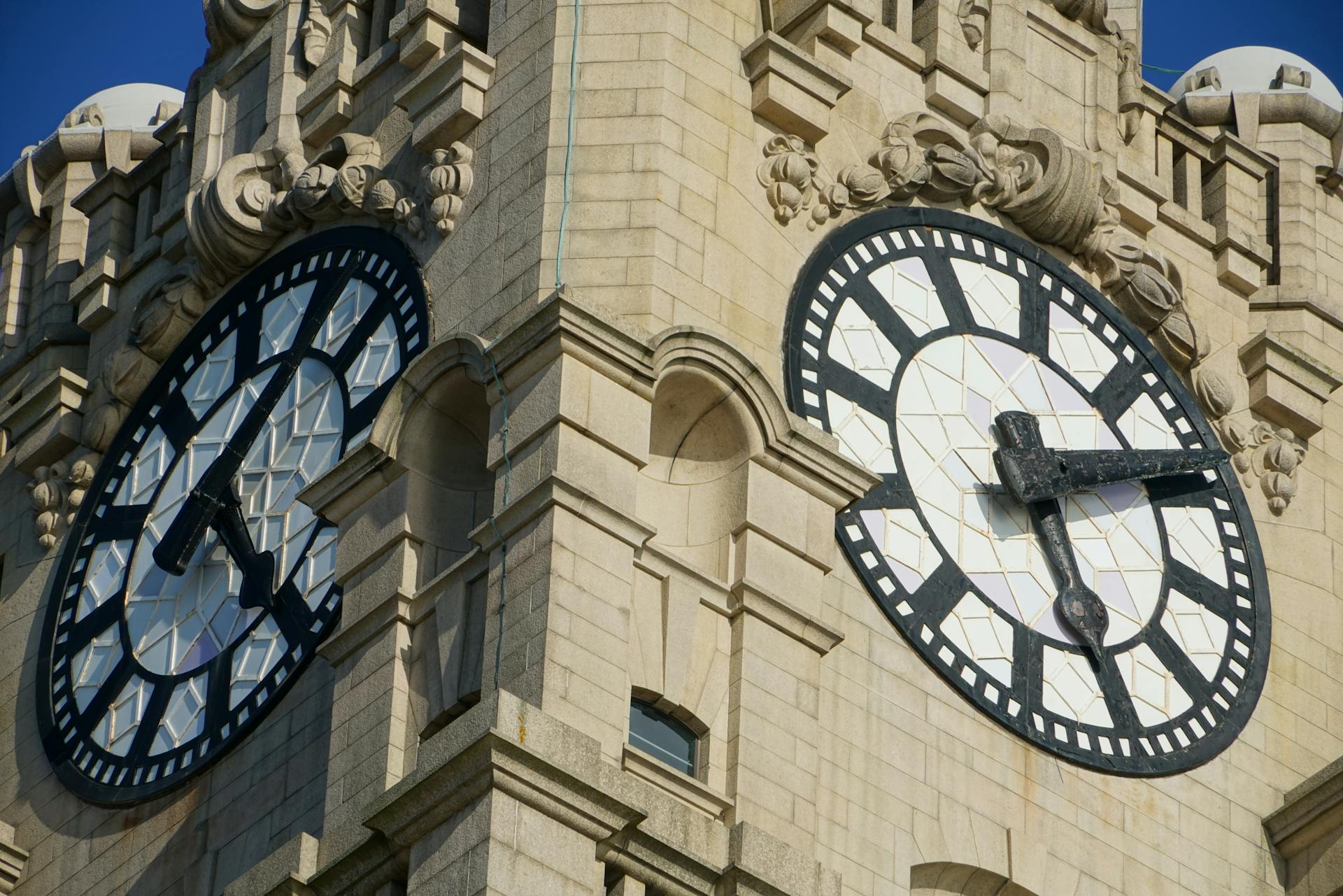 Detailed view of ornate clock faces on a historic stone tower captured in bright sunlight.