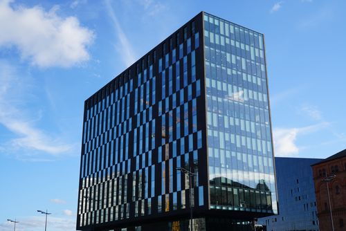Free Tall glass office building reflecting blue sky with scattered clouds. Stock Photo