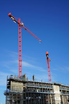 Dynamic view of red tower cranes working at a construction site under blue skies.