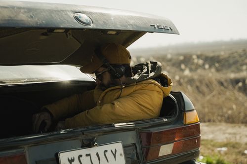 Free A man wearing headphones sits in the trunk of a car outdoors on a sunny day. Stock Photo