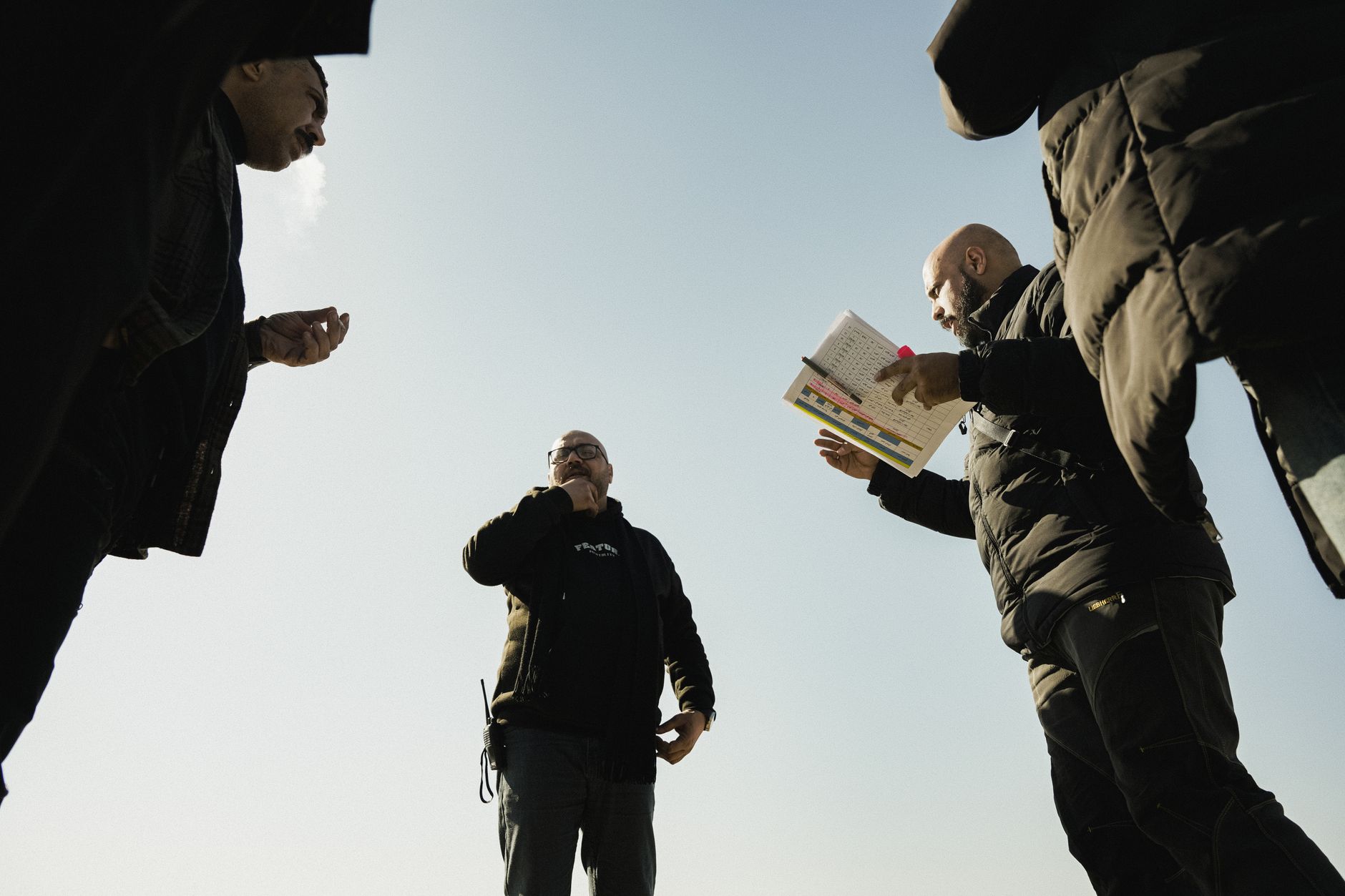 Group of men discussing something outdoors with notes and gestures.