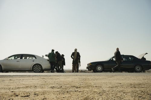 Free People gathered near two cars on a desert road, clear sky above. Stock Photo