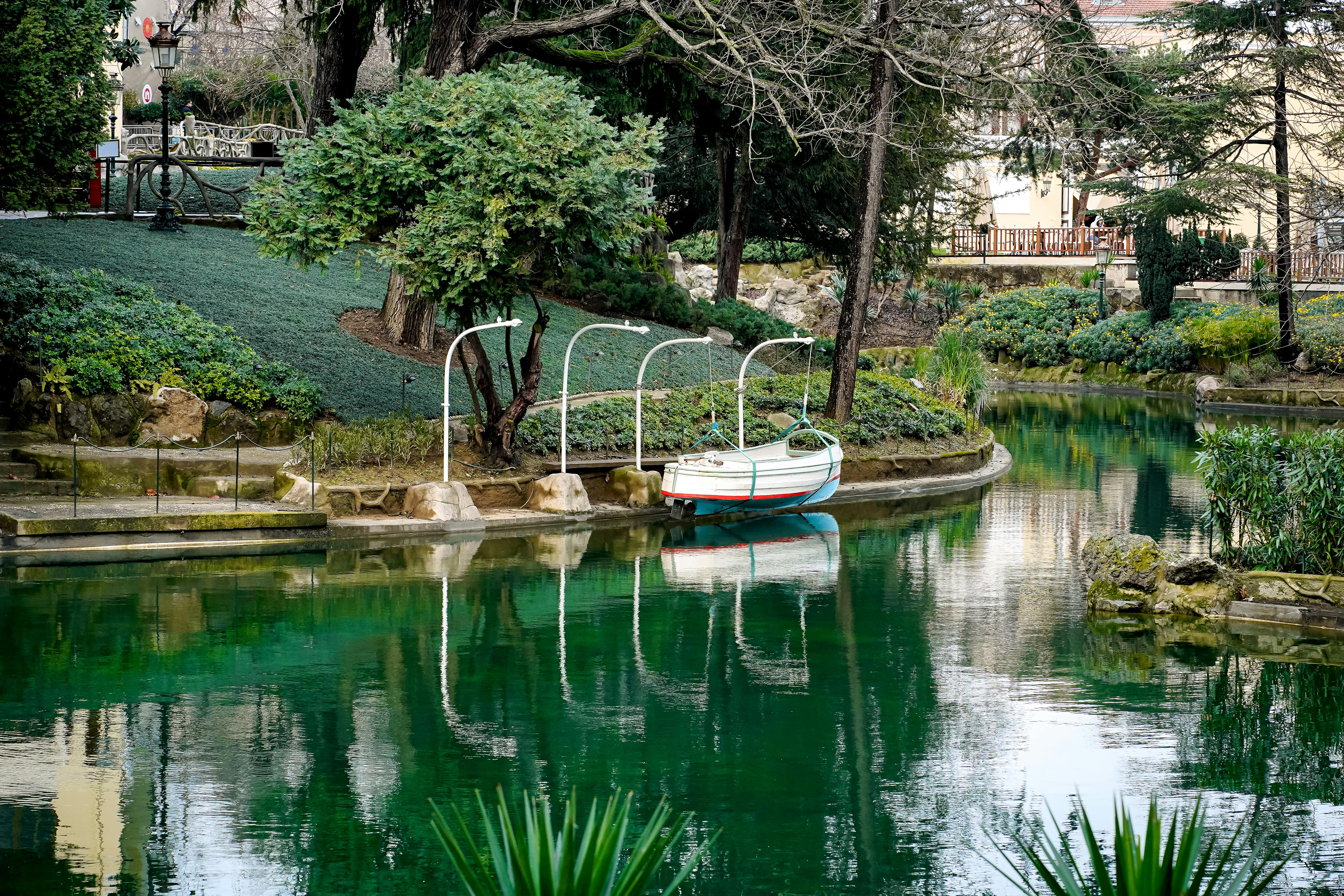 A peaceful green lake with a small boat docked near lush greenery in a tranquil park setting