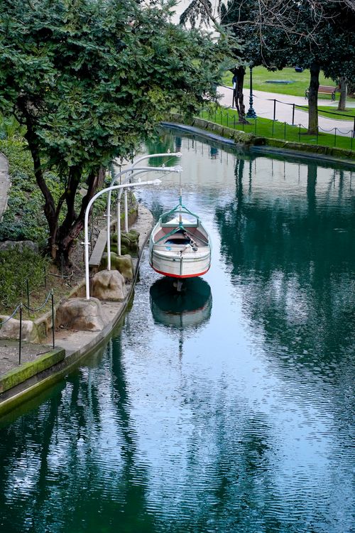 Free A solitary boat peacefully docked on a calm canal, surrounded by lush greenery in a park setting. Stock Photo