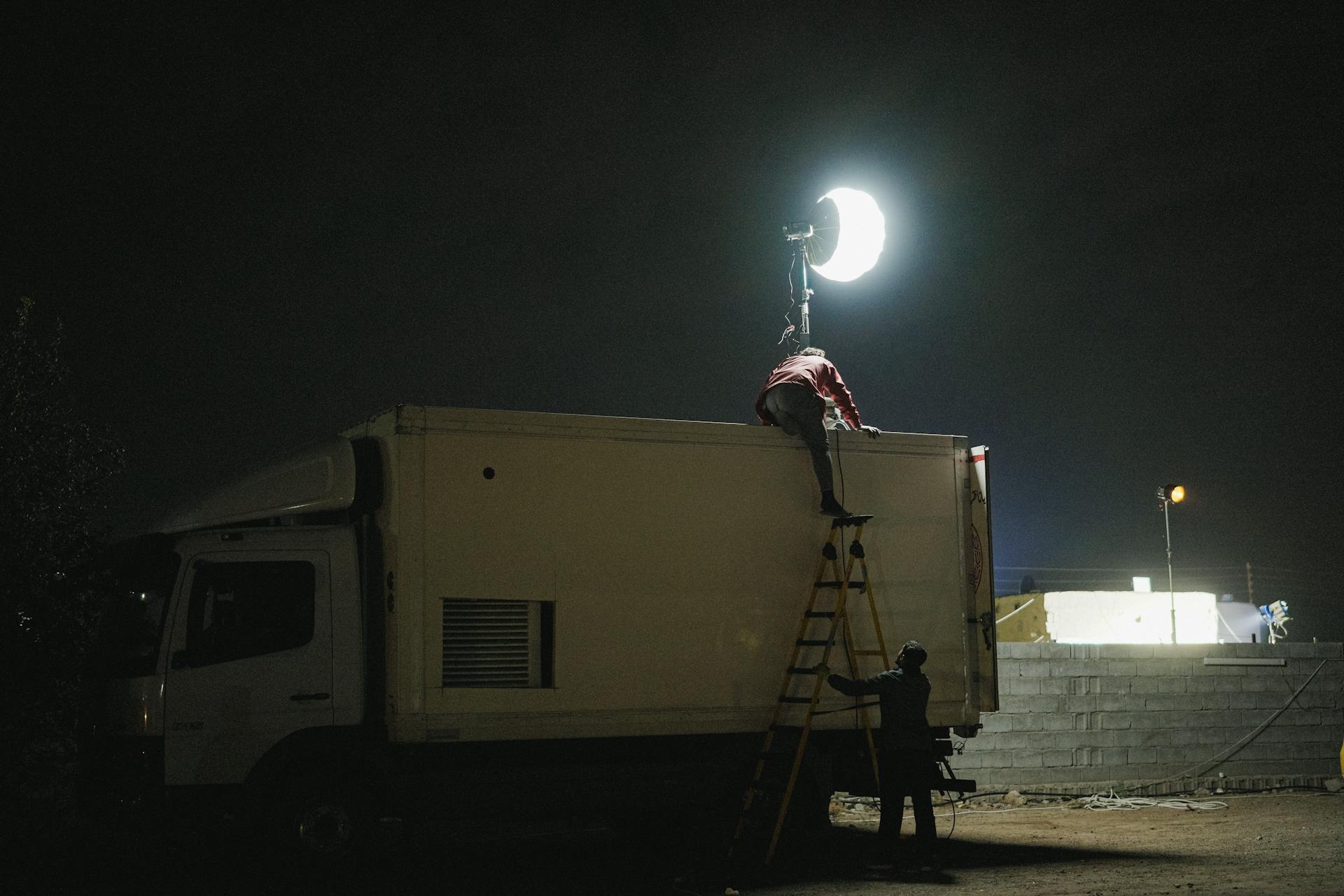 Film crew setting up lighting equipment on a truck at night for movie production.