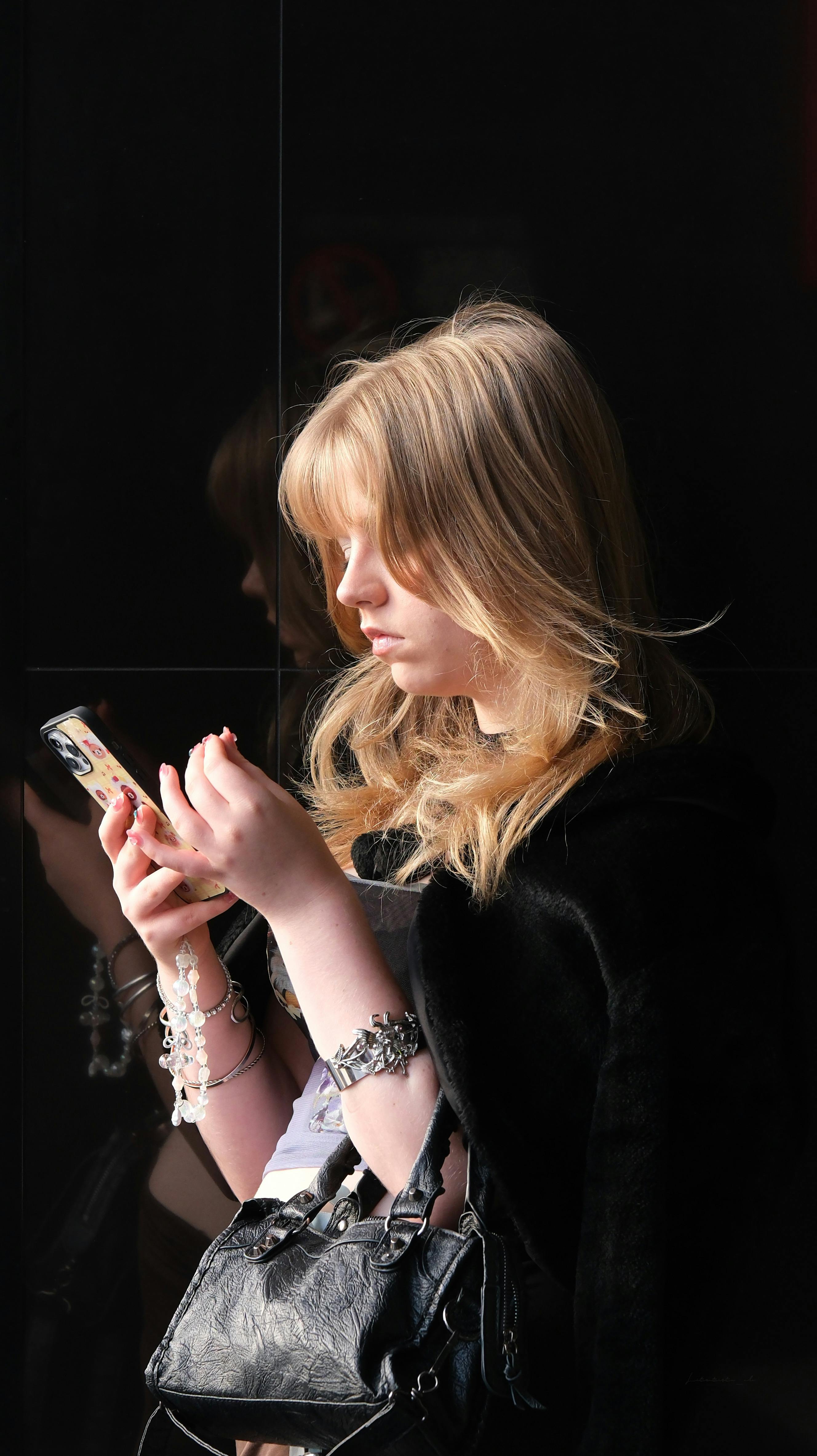 Kostenlos Eine junge Frau konzentriert sich vor einem dunklen Hintergrund auf ihr Smartphone. Stock-Foto