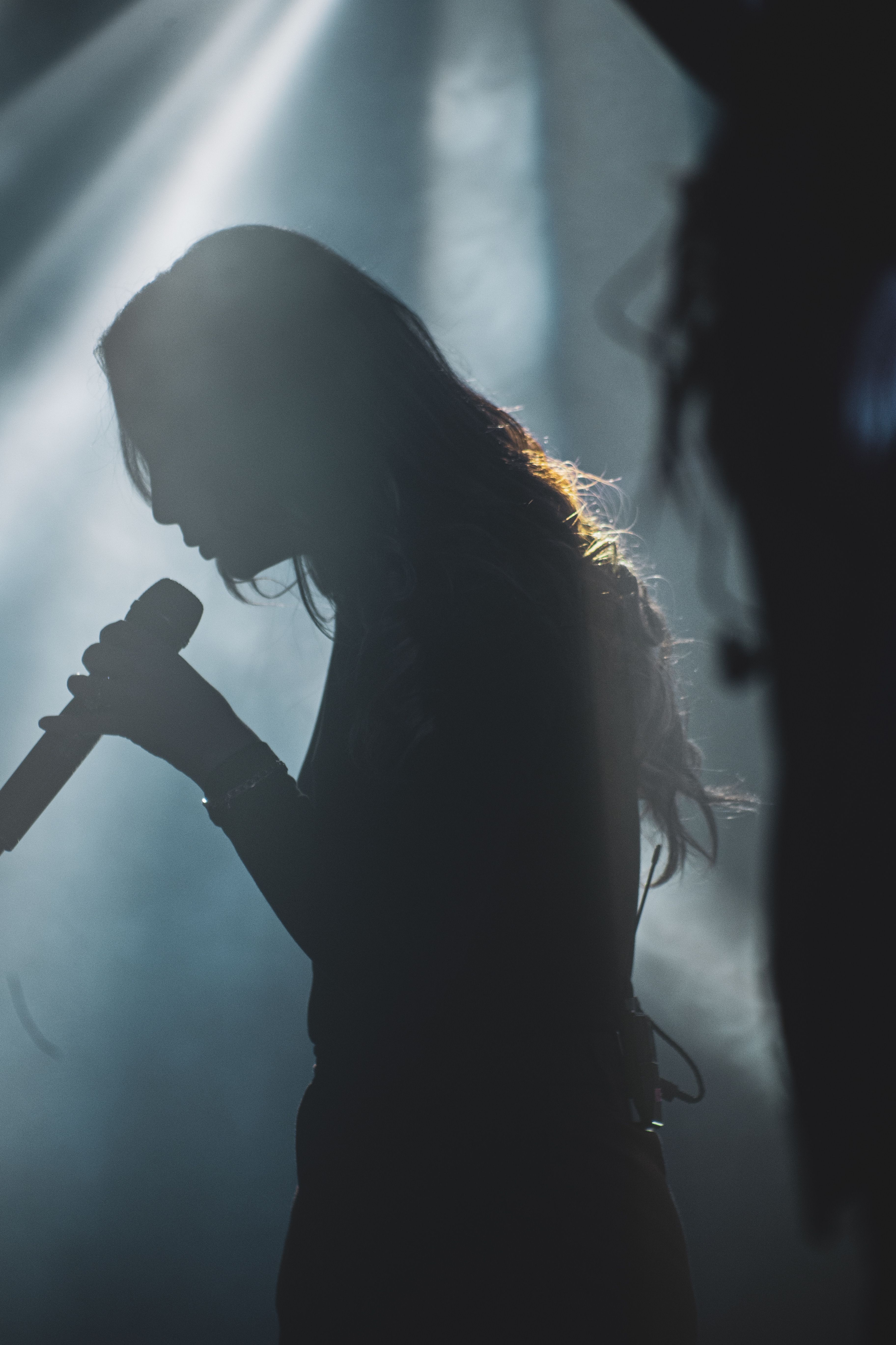 A singer silhouetted against dramatic stage light, microphone raised