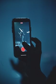Silhouette of hand recording live music performance on a smartphone.