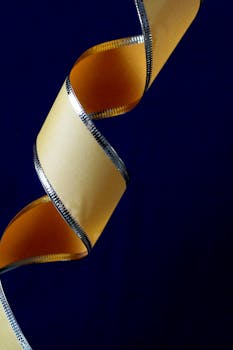 Curled yellow film strip with silver edges against a dark blue backdrop, creating an abstract visual effect.