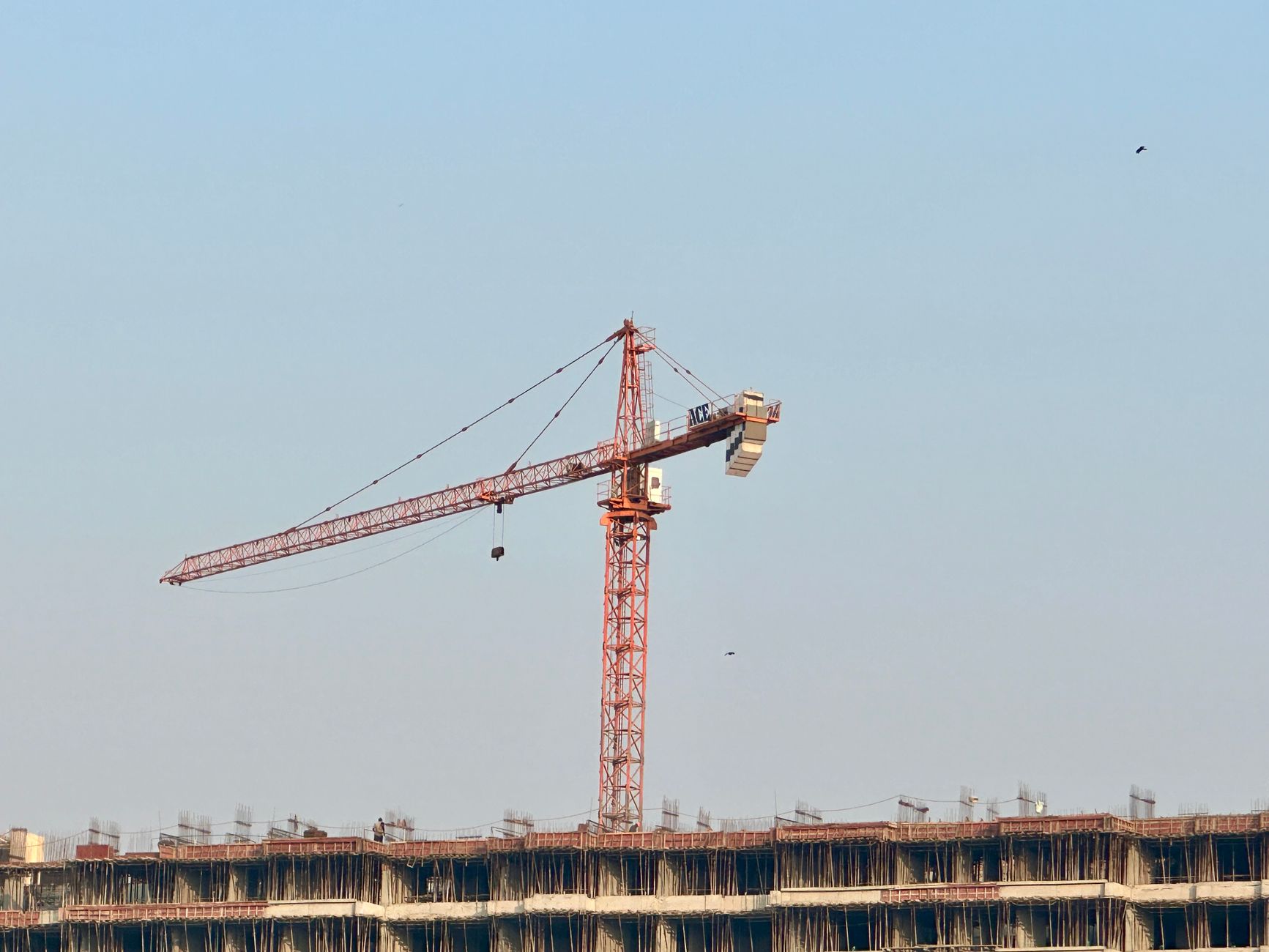 Red tower crane at an urban construction site against a clear blue sky in Mumbai.