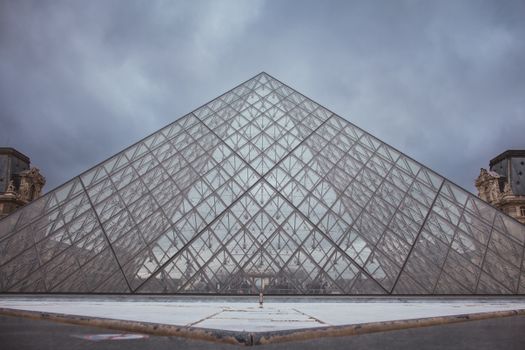 The Louvre Pyramid stands majestically in Paris, showcasing modern architecture against a cloudy sky.