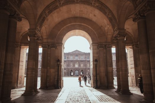 Vintage capture of the Louvre Museum through stone arches, Paris sunlight.