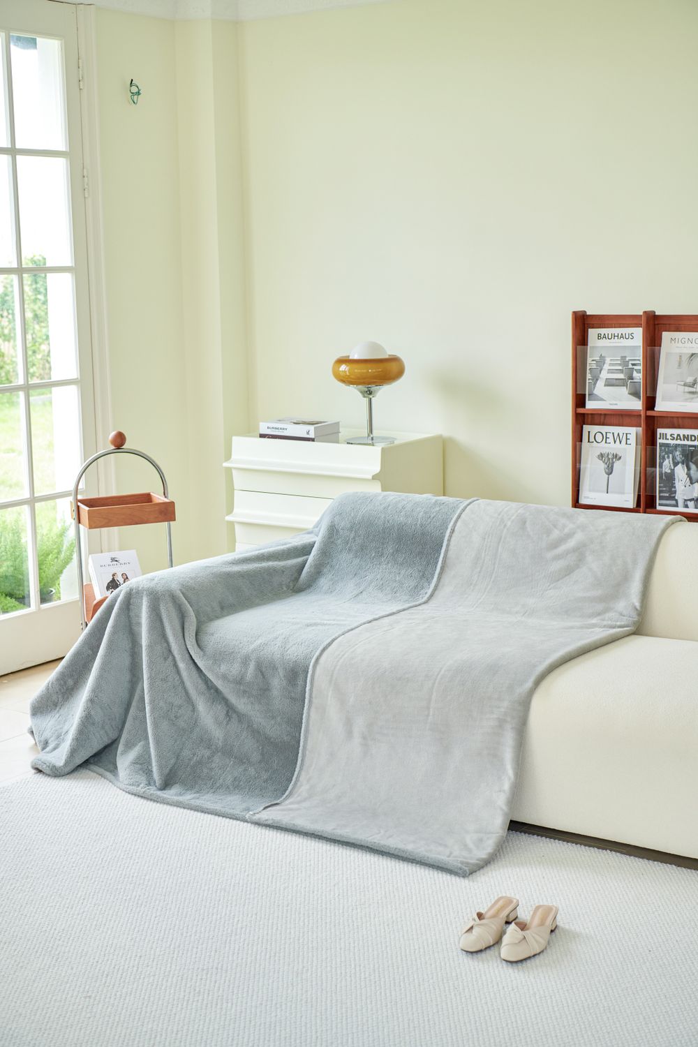 A gray throw blanket draped over a white sofa in a bright room