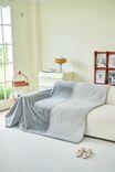 A gray throw blanket draped over a white sofa in a bright room