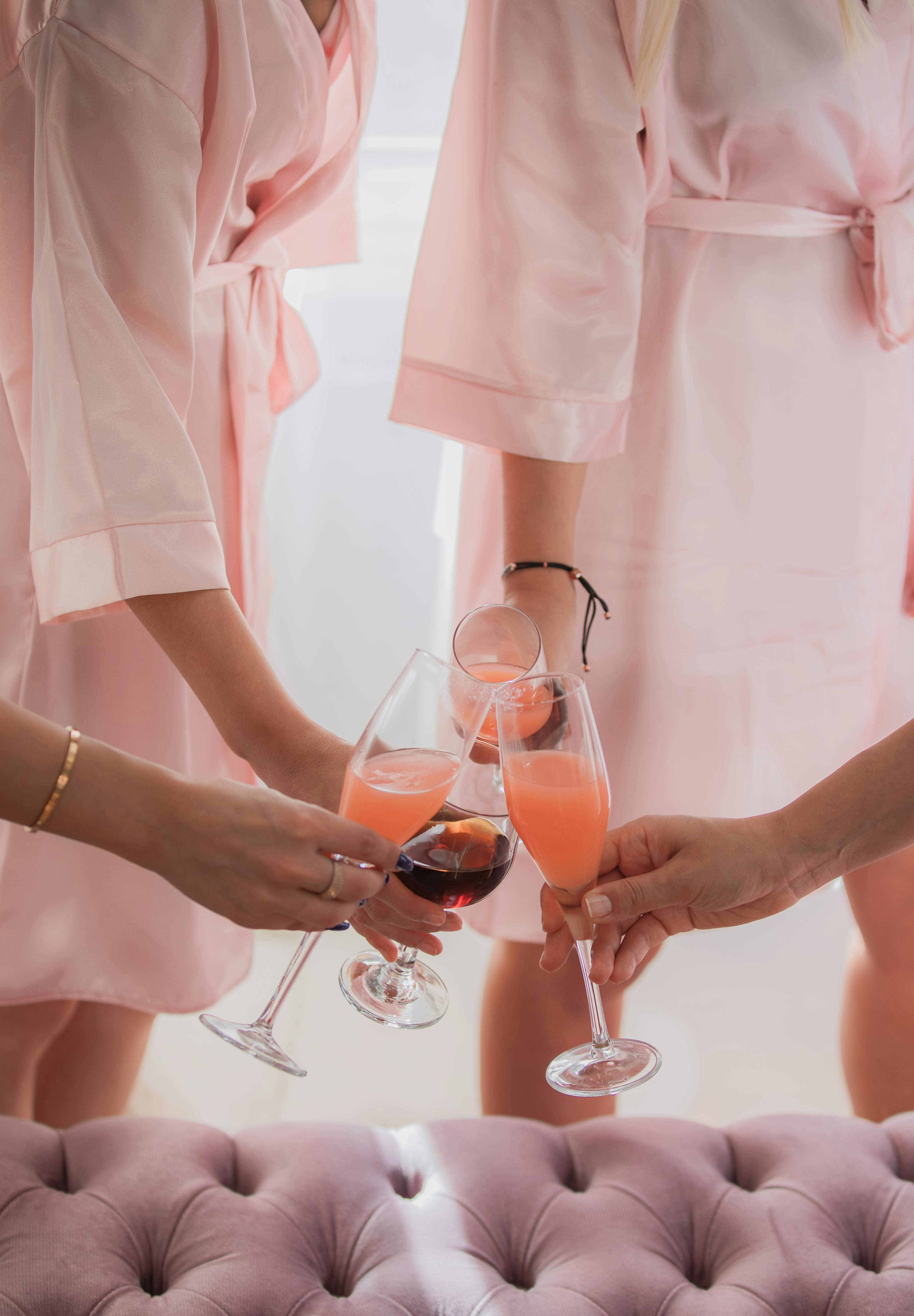 Women in pink robes clinking glasses of cocktails during a bridal party.