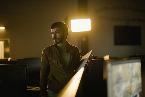 Free A man stands in a dimly lit office holding files, illuminated by a soft light. Stock Photo