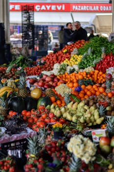 Colorful array of fruits and vegetables at an outdoor market with people in background.