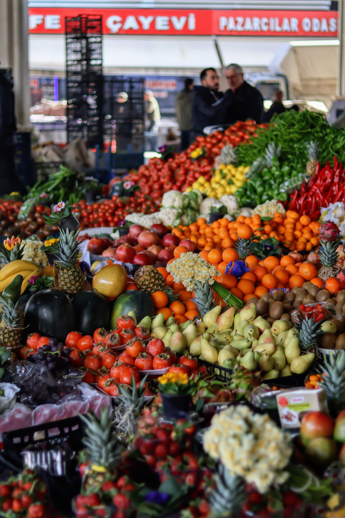 Free Colorful array of fruits and vegetables at an outdoor market with people in background. Stock Photo