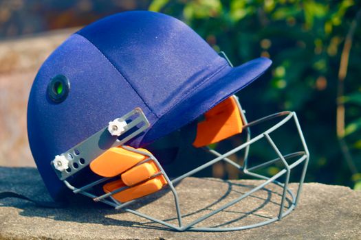 Close-up of a blue cricket helmet with faceguard placed outdoors on a sunny day.