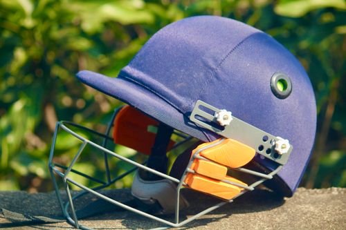 Free A blue cricket helmet placed outdoors with lush greenery in the background, showcasing sports equipment. Stock Photo