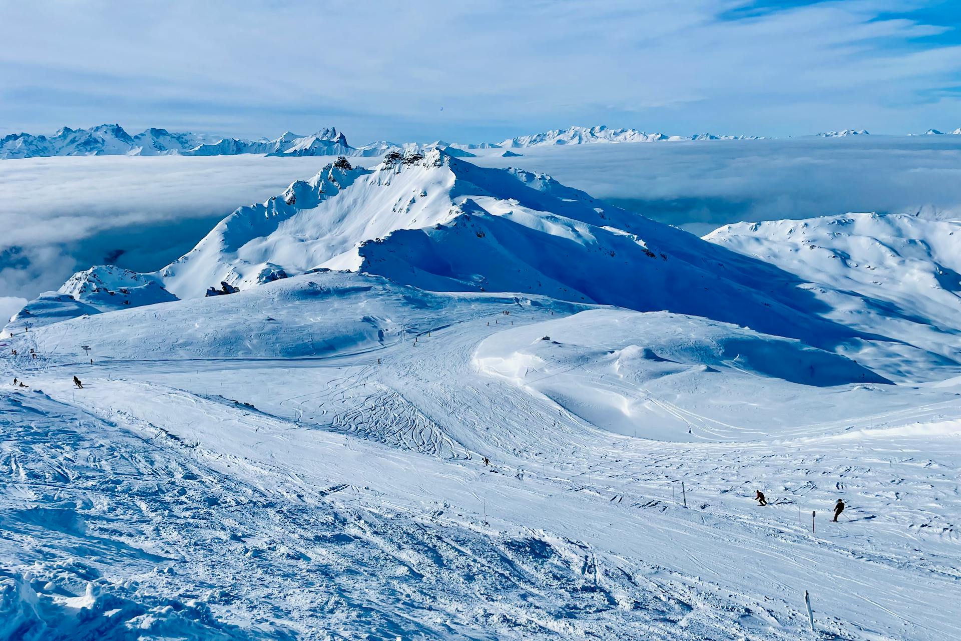 Breathtaking snowy mountain landscape at a ski resort with skiers and clear blue skies.