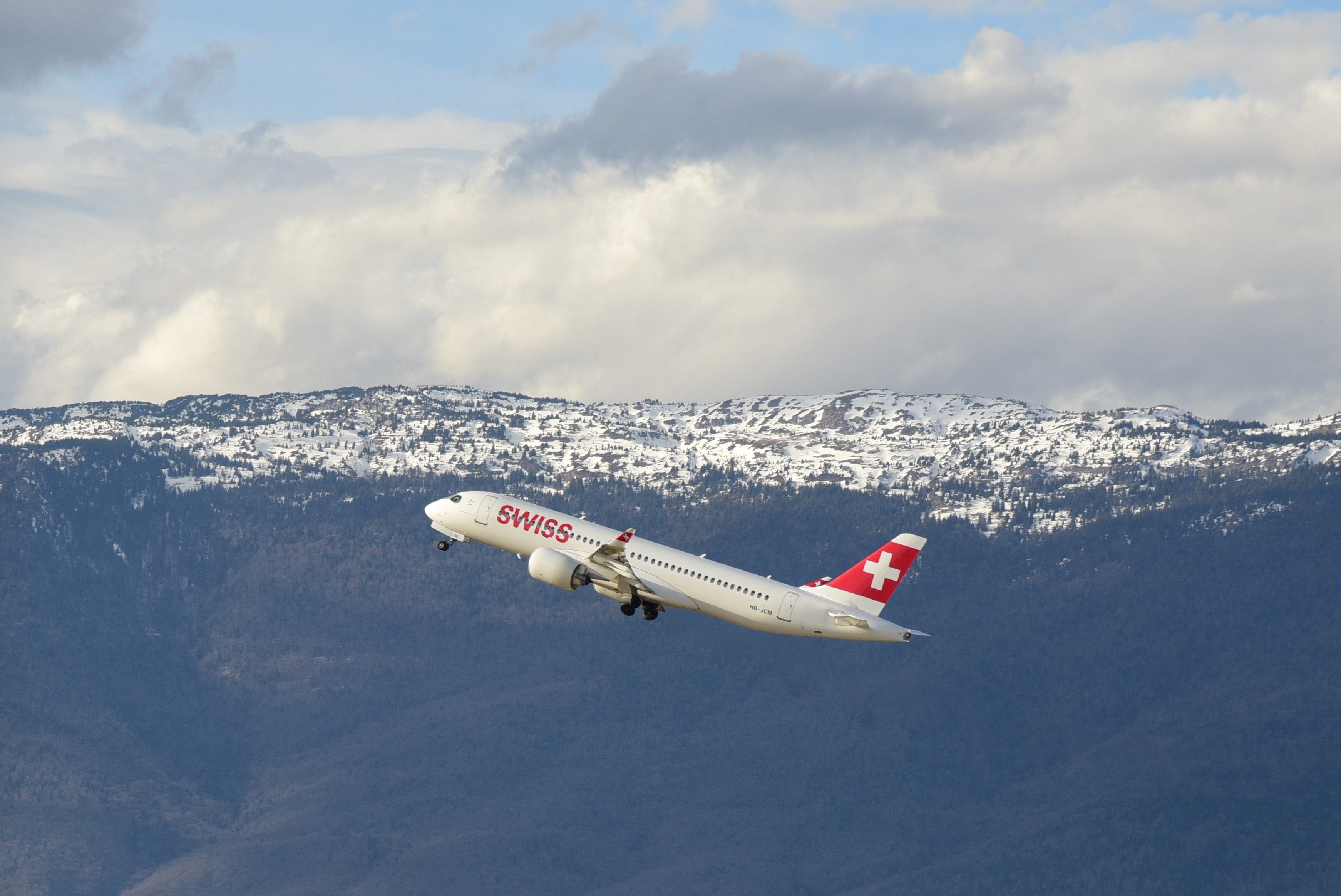 A Swiss airplane taking off with snow-capped mountains in the background in Geneva, Switzerland.