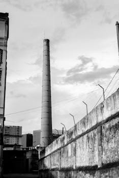 Monochrome view of a tall factory chimney in an urban setting with dramatic clouds.
