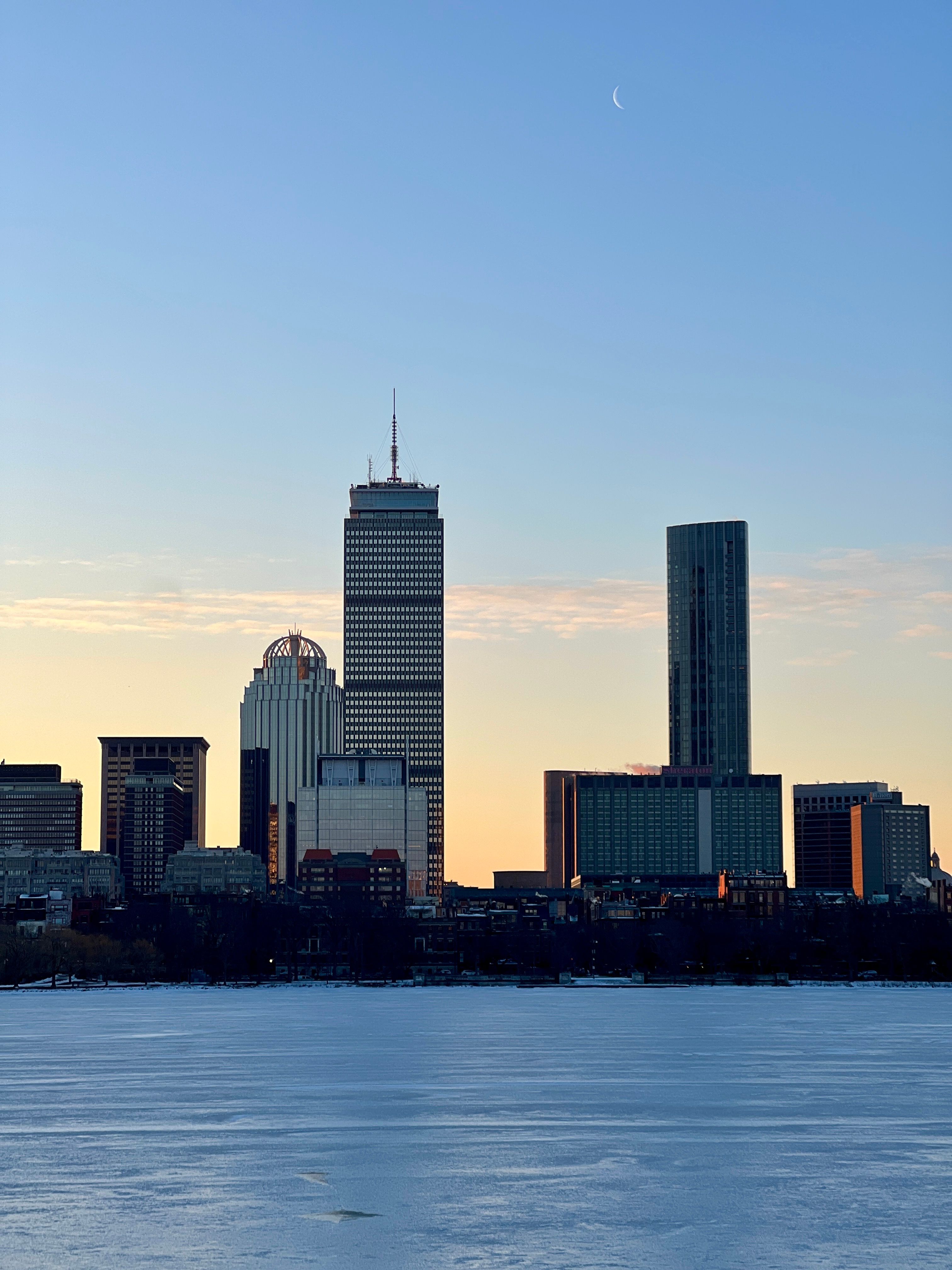 Boston skyline featuring the Prudential Center during a serene dusk with a crescent moon.