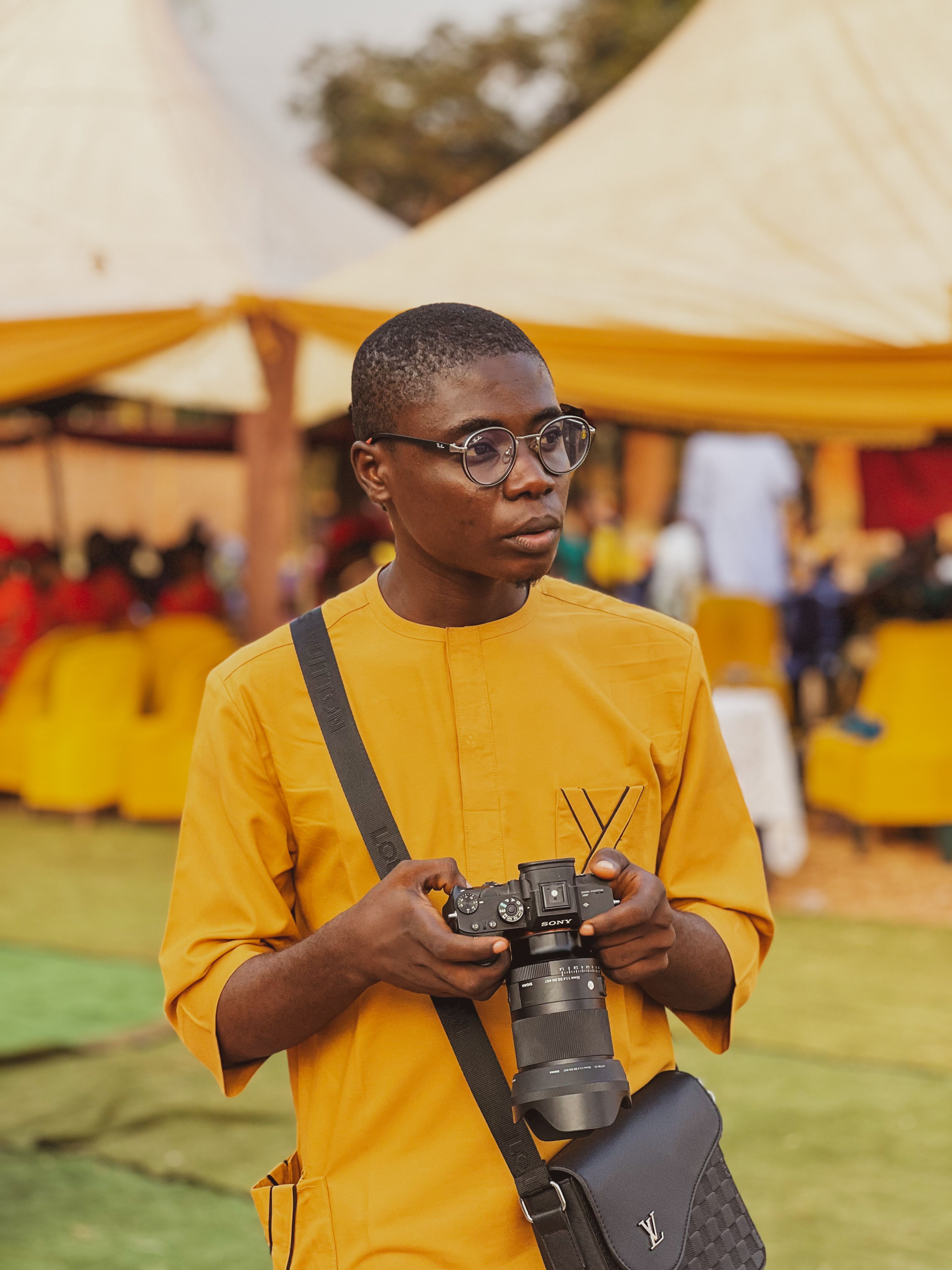 Young man holding a camera at a lively outdoor gathering in Nigeria