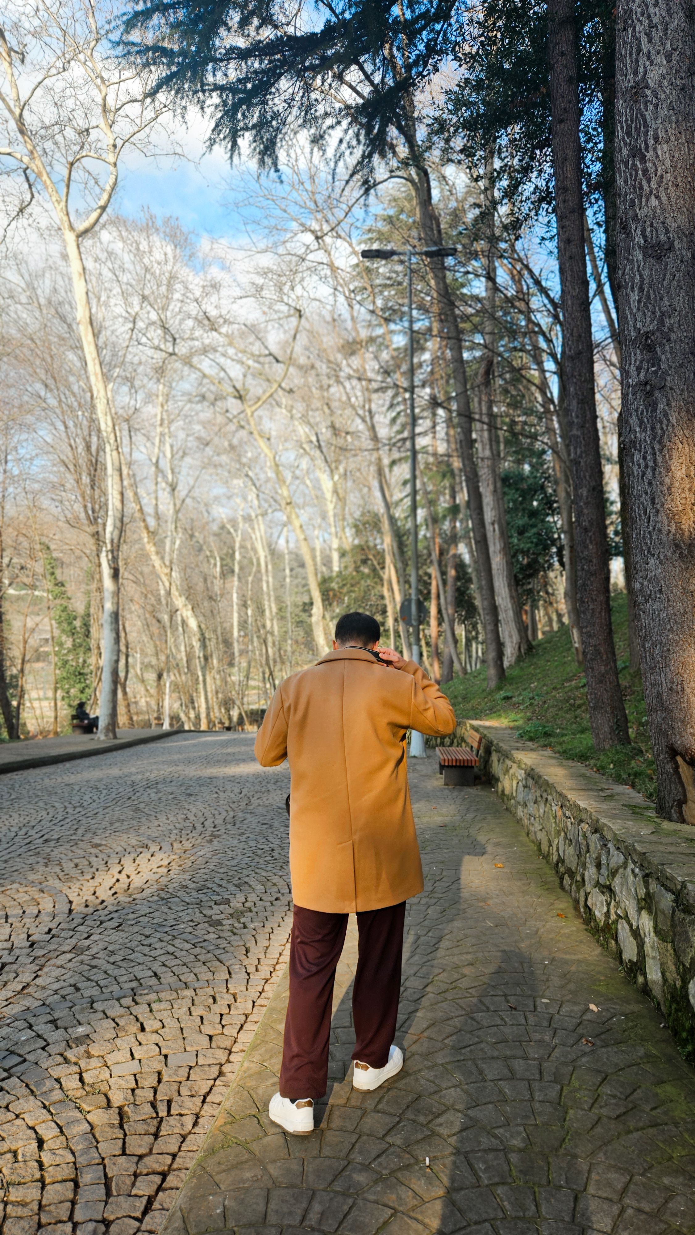 Man in a coat walking down a cobblestone path in a winter park.