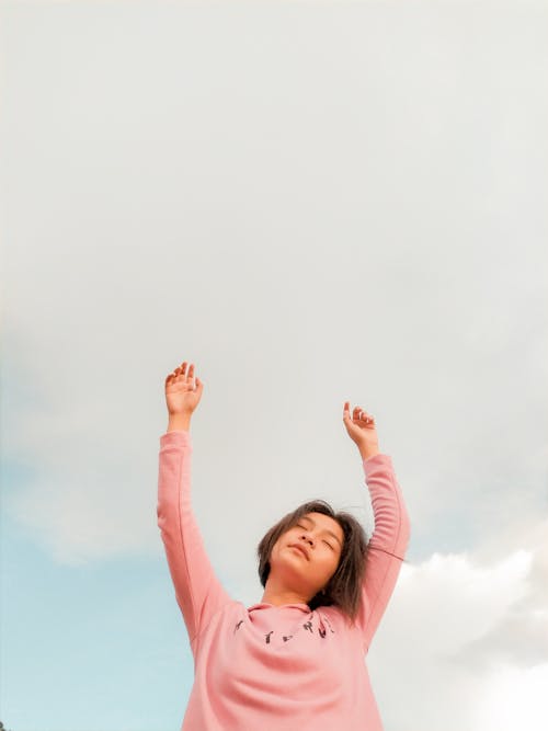 Free Low-Angle Shot of a Woman in a Pink Long Sleeve Shirt Raising Her Hands Stock Photo