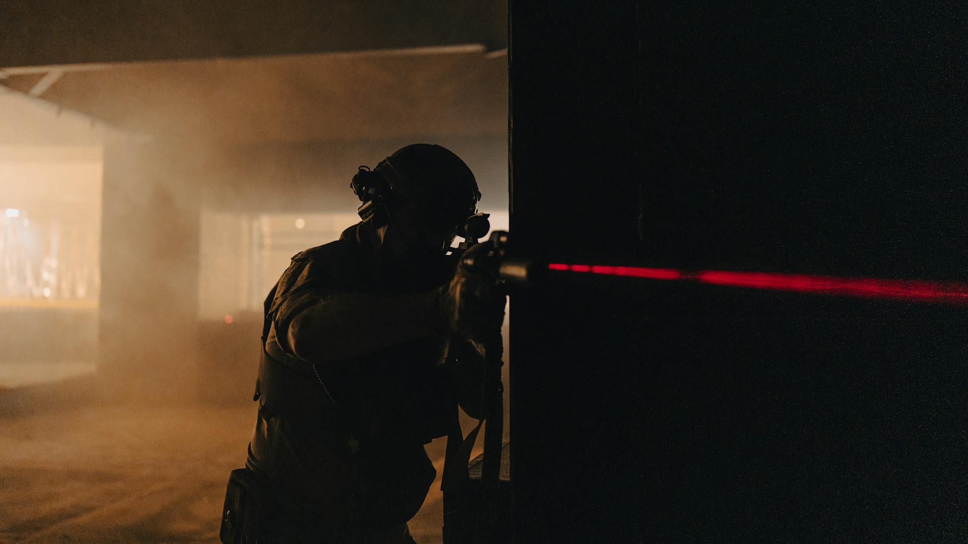 A soldier with night vision aiming with a laser sight in a dark, smoky room.