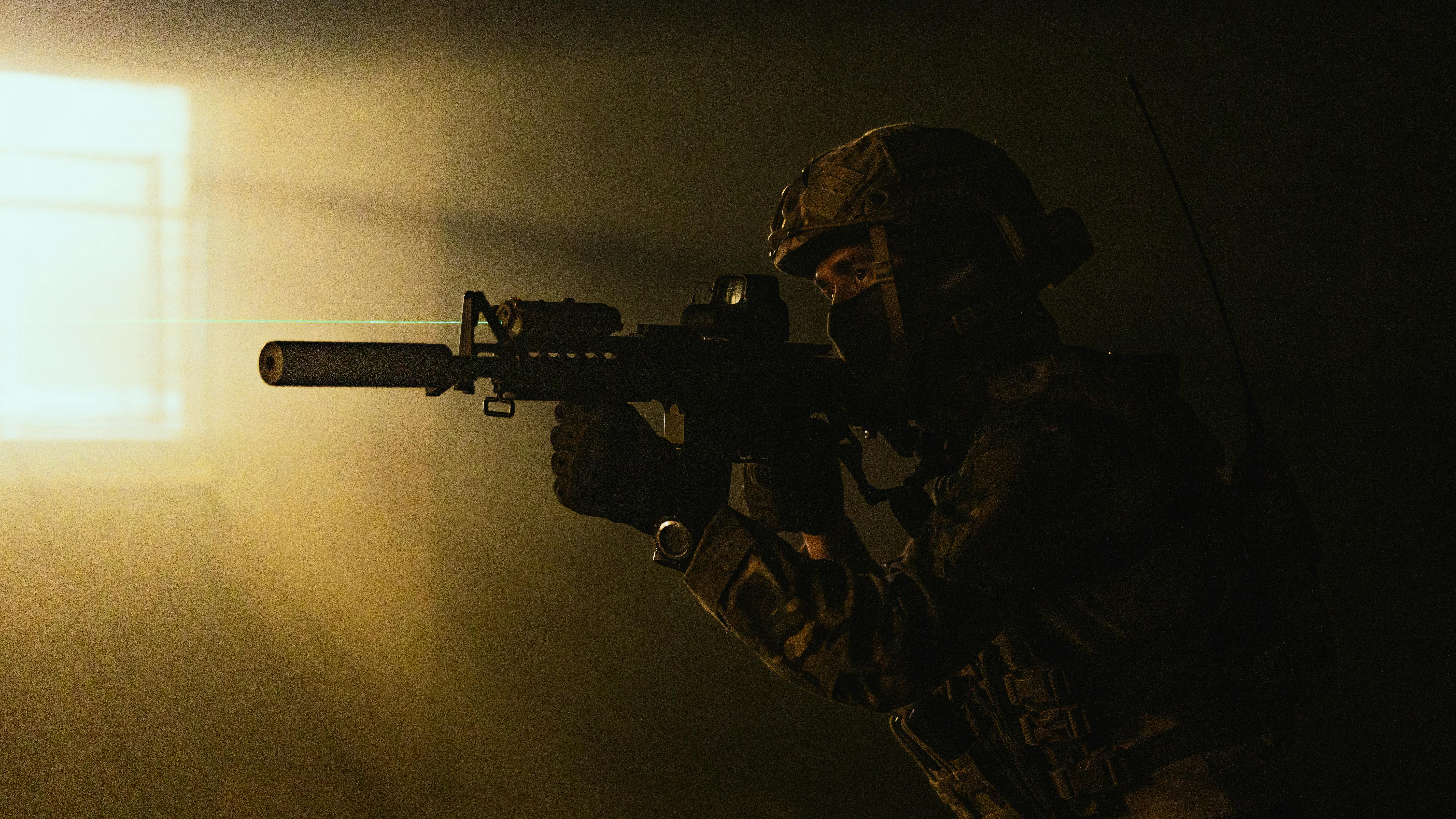 A soldier in tactical gear aims a weapon with a laser sight in low light conditions. Prescription Goggle Inserts - A soldier in tactical gear aims a weapon with a laser sight in low light conditions.
