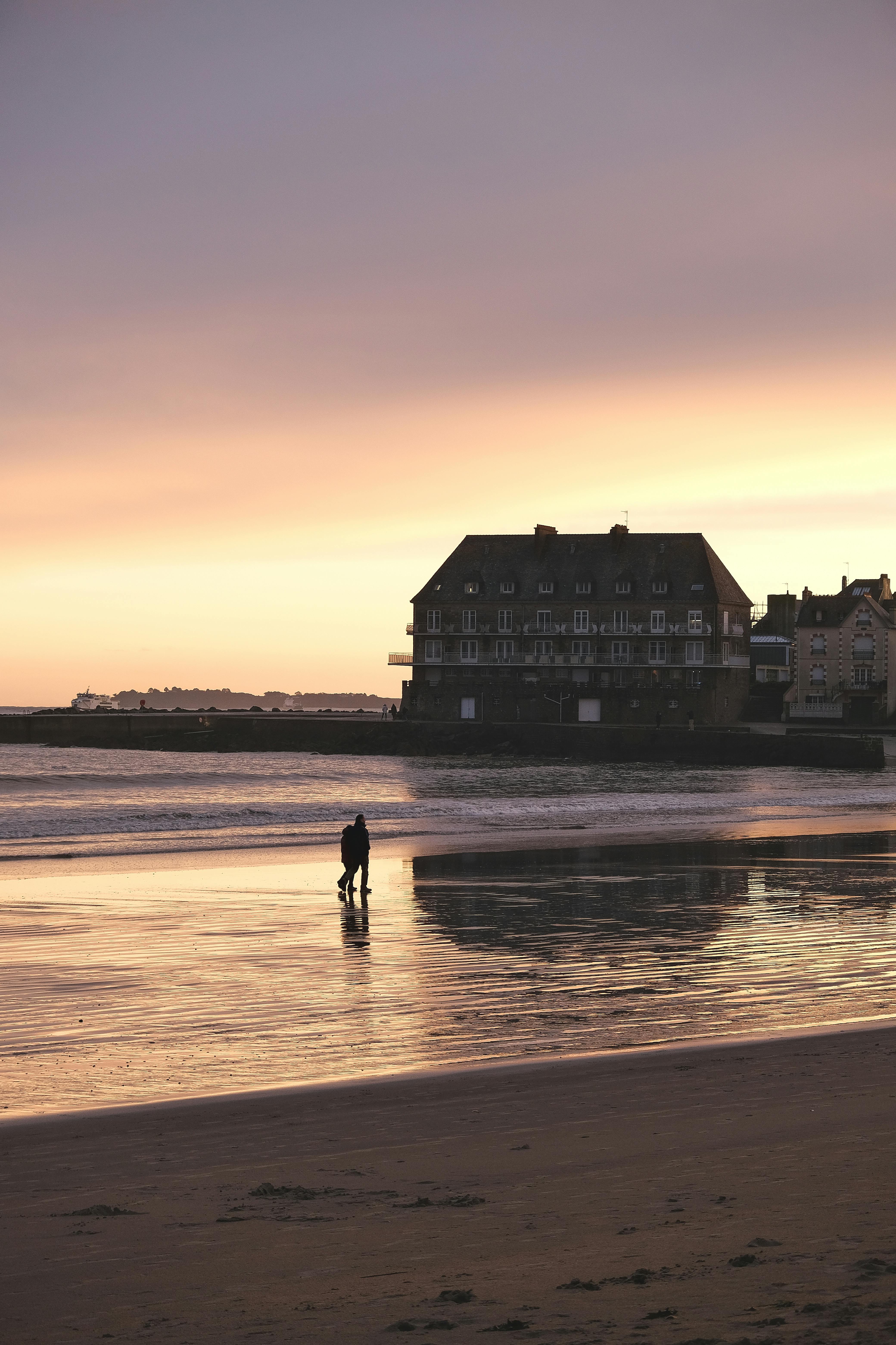 Peaceful beach scene with silhouetted figures during sunset in Brittany, France.