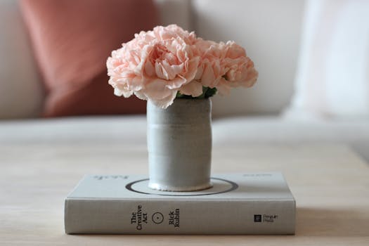 Photo by Julia Olson A vase of pink carnations elegantly placed on a book indoors.