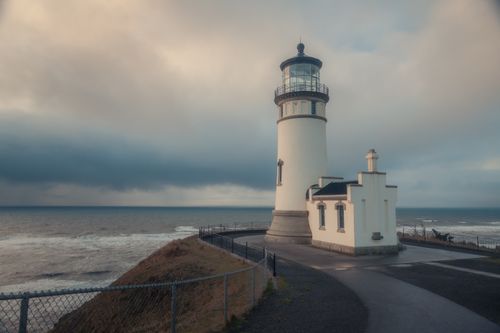 Free Peaceful scene of a historic lighthouse by the ocean under dramatic clouds. Stock Photo
