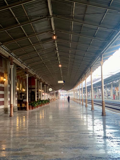 Free An empty railway platform under a covered roof with a lone person walking away. Stock Photo