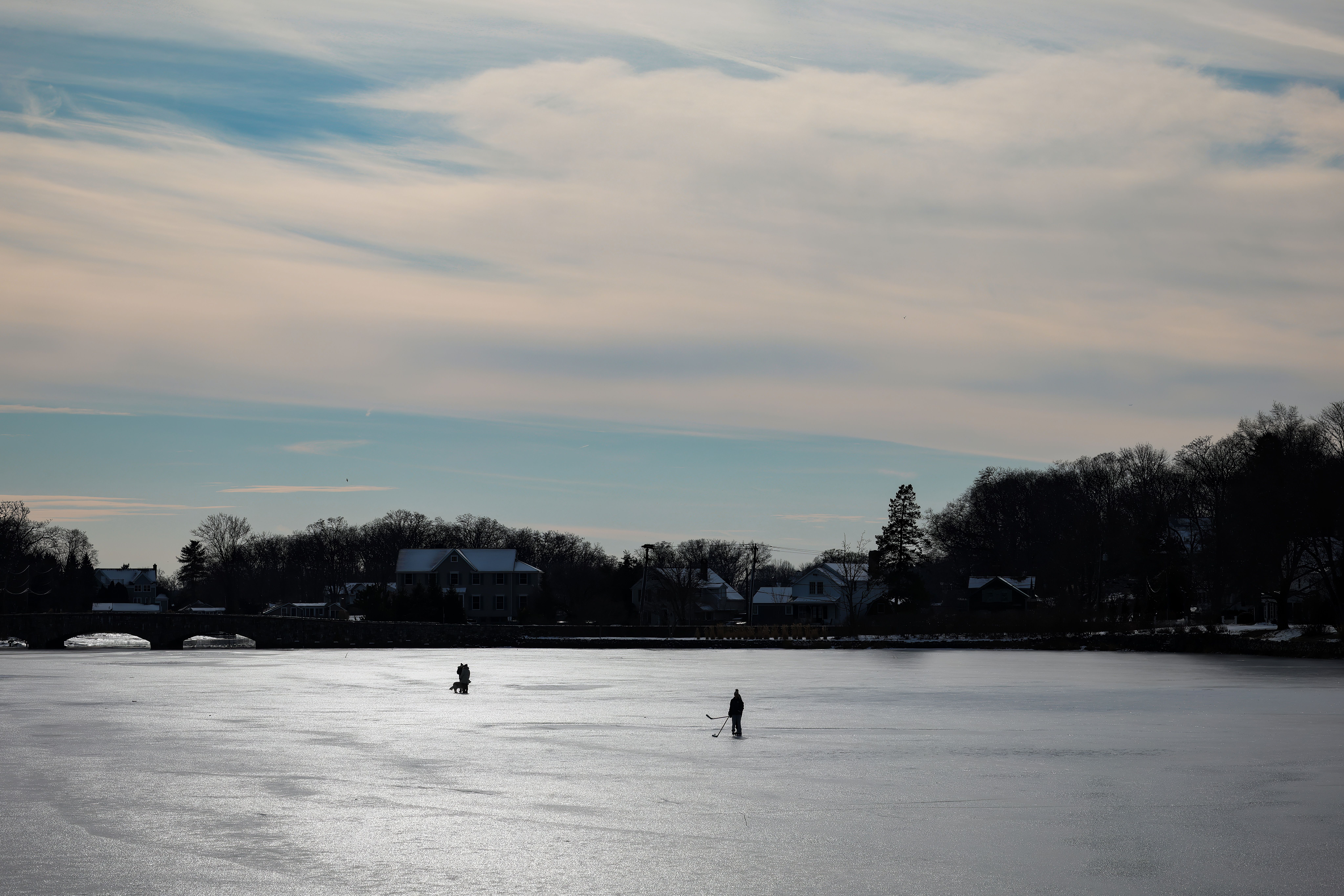 Two people playing ice hockey on frozen Gorham's Pond, Darien, CT, under a winter sky.