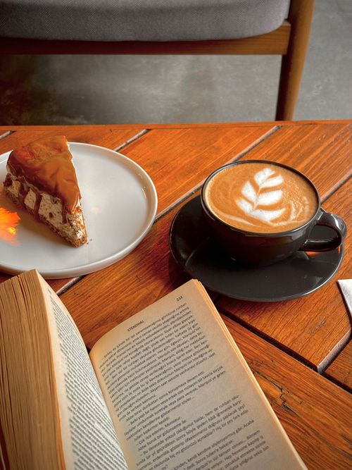 Free A warm and inviting café setting featuring a latte, cake slice, and open book. Stock Photo