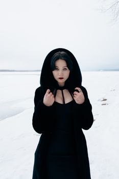 A woman in a black coat standing against a snowy landscape, exuding an enigmatic aura.