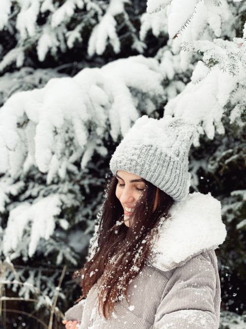 Free Smiling woman in winter attire amidst snow-covered trees during a winter day. Stock Photo