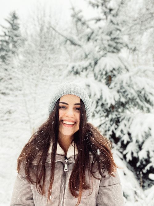 Free Young woman smiling in a snowy forest, wearing a gray beanie and winter coat. Stock Photo