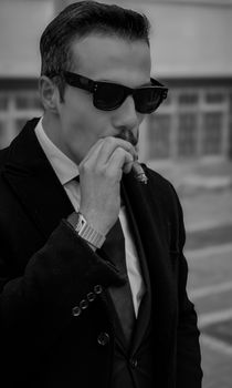 Elegant man in a suit and sunglasses smoking a cigar, exuding sophistication and class.