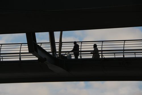 Free Silhouetted figures on a modern bridge against a cloudy sky, showcasing urban travel. Stock Photo