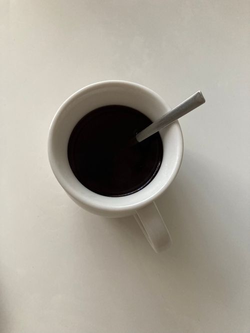 Free White mug filled with black coffee and a spoon on a plain surface. Stock Photo