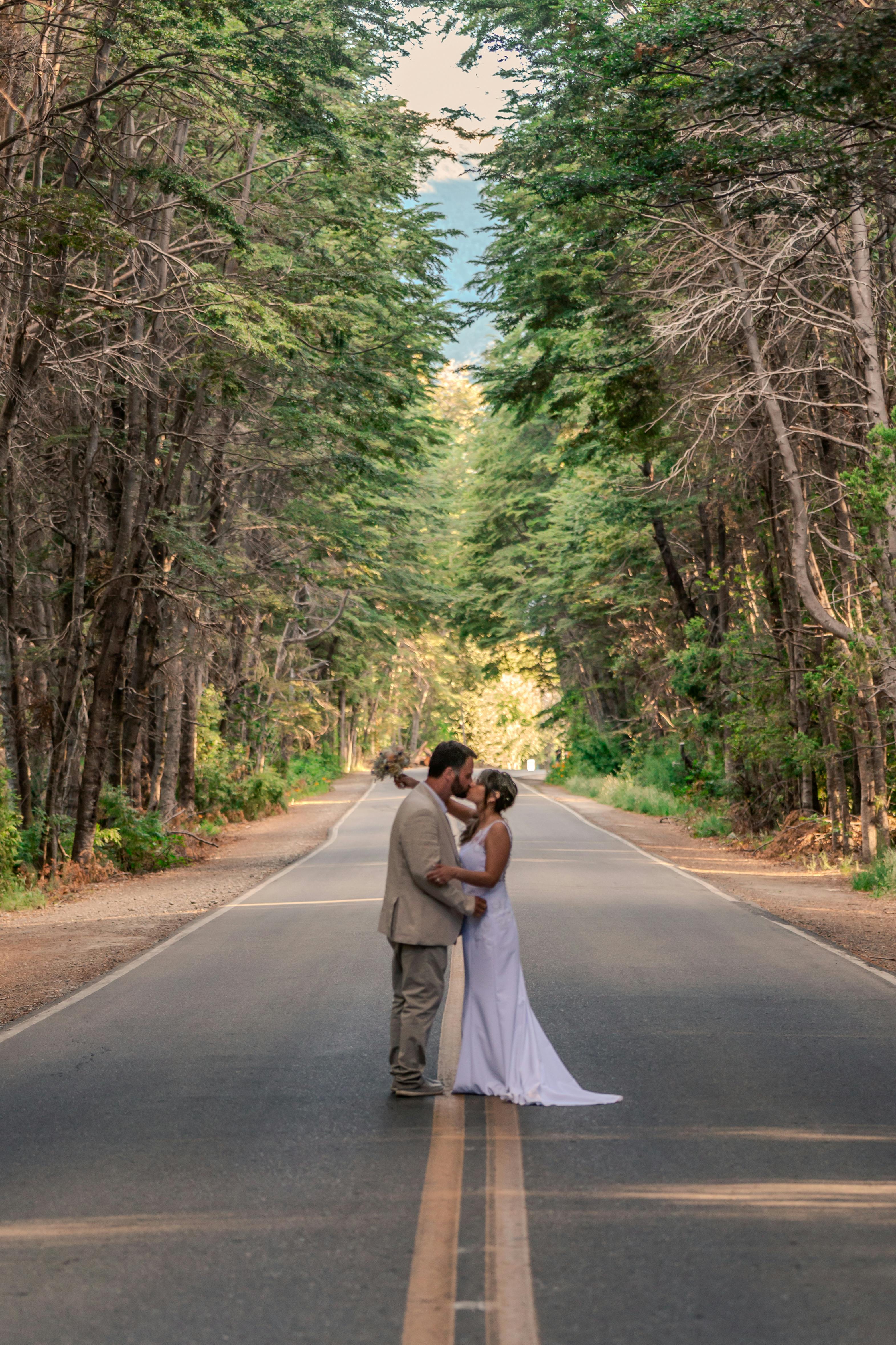 Couple shares a romantic kiss on a serene forest road in Bariloche, Argentina.