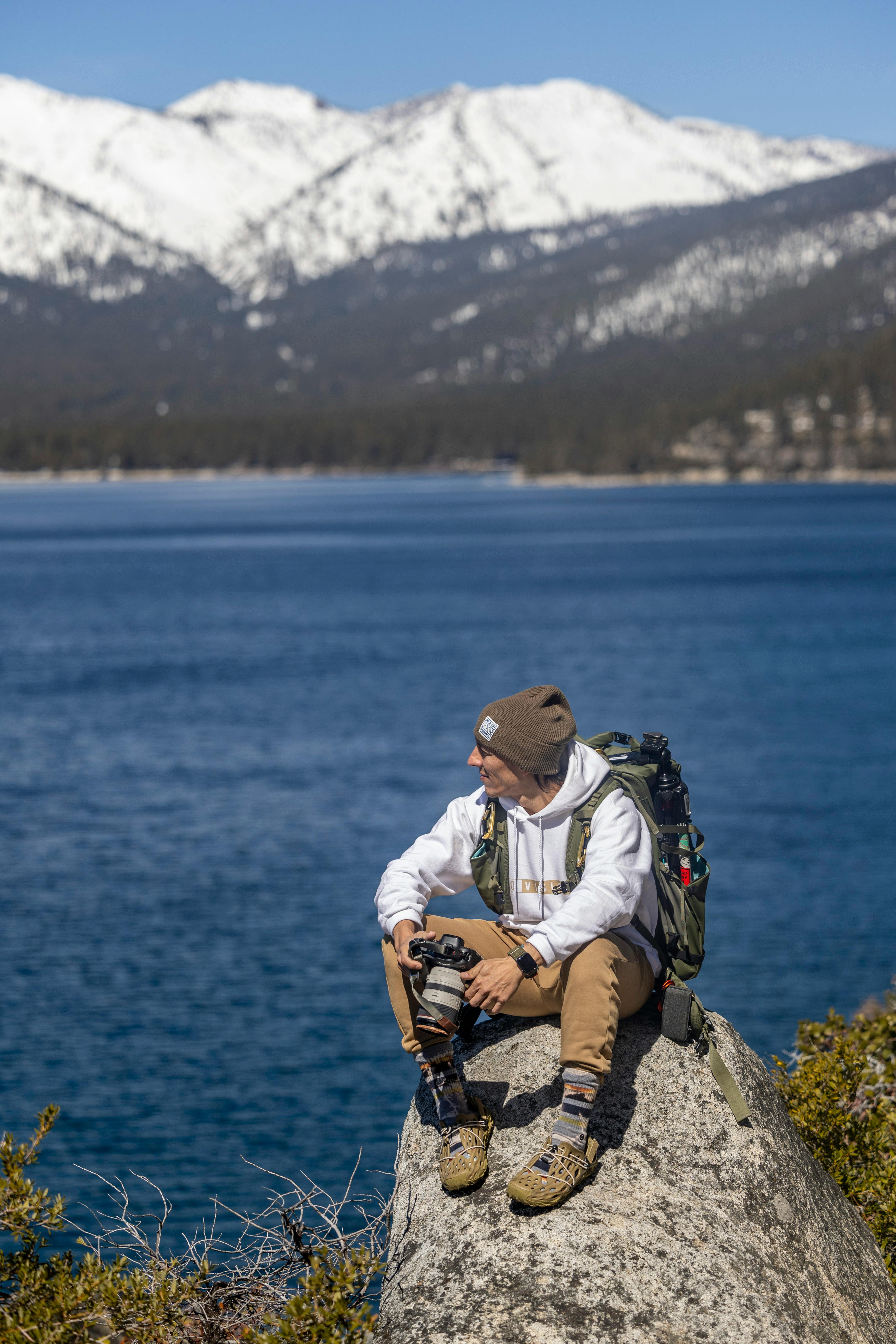 A hiker enjoys a serene view of Lake Tahoe with snow-capped mountains in the background.